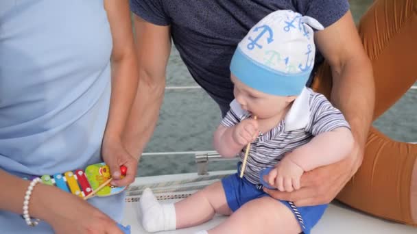 Teething at baby which bites toys outdoors, good father with mother takes care of son on pleasure boat, — Stock Video