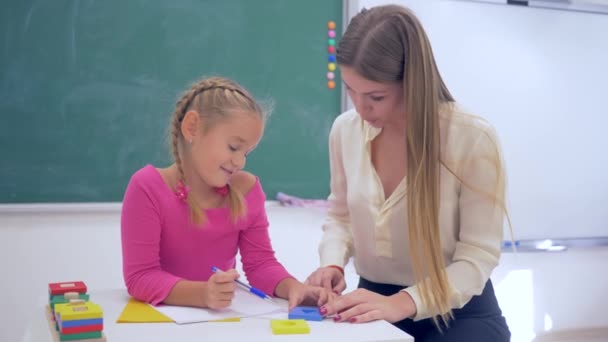 Вчителька, жінка-вчителька допомагає вченим дівчатам набувати інформацію, використовуючи пластикові фігури за столом біля дошки в класі школи — стокове відео