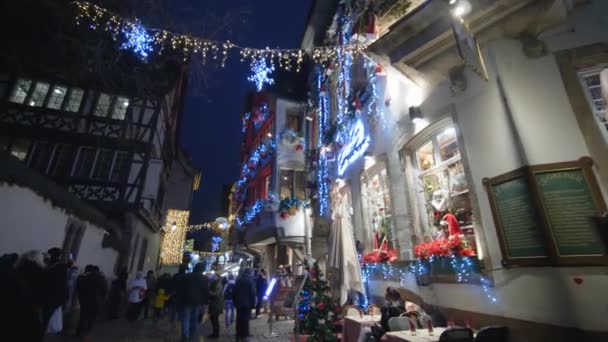 New Year mood in city, lot of tourists people are walking on Christmas Eve on street decorated with bright garlands and toys on houses in evening — Stock Video