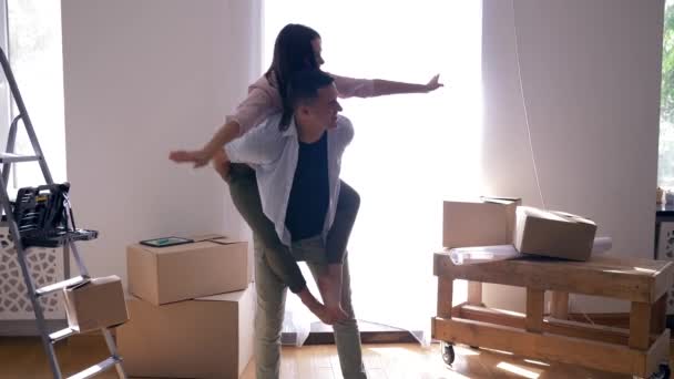 Laughing woman sitting on back of boyfriend and spinning among boxes during relocation to housing — Stock Footage Laughing woman sitting on back of boyfriend and spinning among boxes during relocation to housing Stock Video