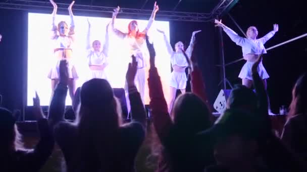 Cantora menina com microfone canta e dança com as meninas no palco na frente de uma multidão de fãs à noite — Vídeo de Stock