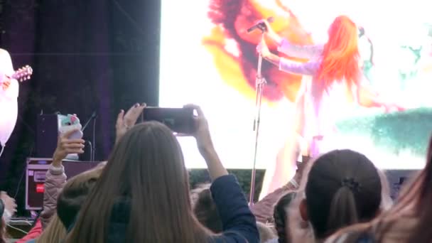 Τραγουδίστρια κορίτσι με κόκκινα μαλλιά τραγουδά στο μικρόφωνο στη σκηνή μπροστά σε ένα πλήθος οπαδών — Αρχείο Βίντεο