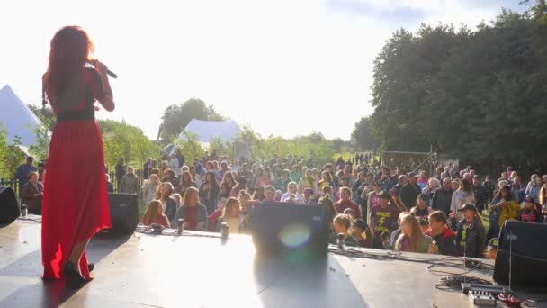 Menina em vestido vermelho cantando em microfone no palco na frente da multidão de pessoas, concerto ao ar livre — Vídeo de Stock