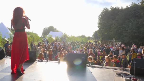 Ragazza in abito rosso cantare in microfono sul palco di fronte alla folla di persone, concerto all'aperto — Video Stock