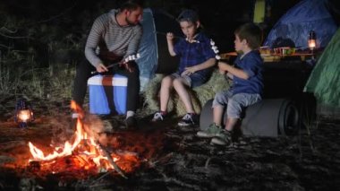 daddy speaks with sons near bonfire into night forest, dad Tells stories for kids in journey with tents,