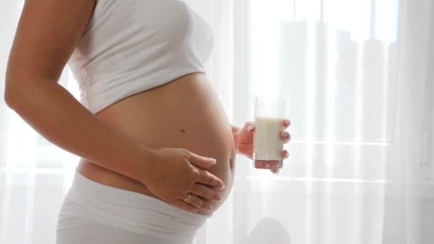 Moederschap, mooie zwangere vrouw drinkt melk uit een glas en wrijven buik — Stockvideo