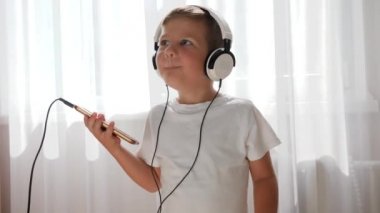 Elinde telefonla gülümseyen çocuk kulaklıkla müzik dinliyor ve odada dans ediyor.