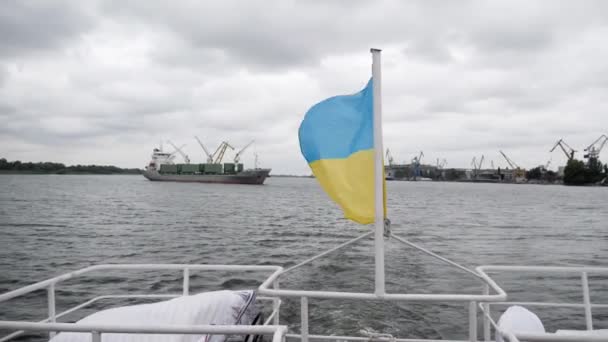 Ukrainian flag flies freely at back of boat on background of seaport with containers and cranes — Stockvideo