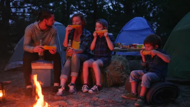 Mujer y hombre beben cerveza y comen maíz amarillo fresco del fuego durante las vacaciones de verano, la familia disfruta del maíz con sal — Vídeo de stock