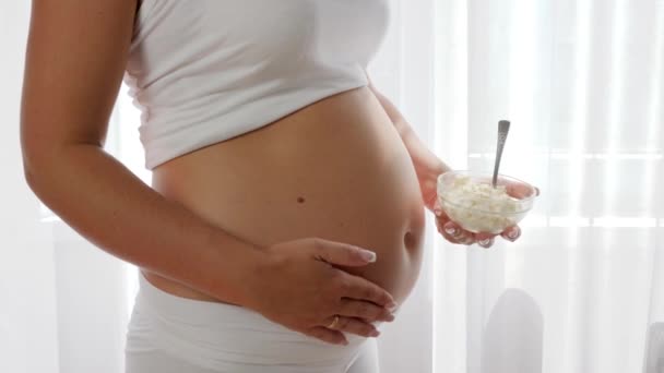 Primer plano plato con cuajada en la mano de una mujer embarazada cerca de una gran barriga desnuda — Vídeo de stock