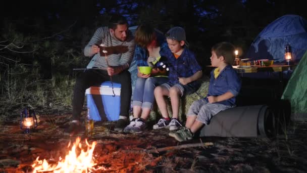 Acampamento, família se comunica e colocando marshmallows no espeto perto de fogo na floresta, marido e esposa — Vídeo de Stock