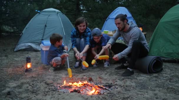 Familia americana Siéntese alrededor de fuego freír maíz amarillo, picnic familiar al aire libre, mamá, niños y papá durante las vacaciones de verano — Vídeos de Stock