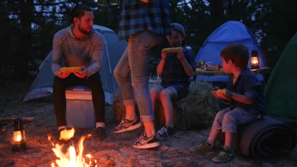 I genitori bevono birra e mangiano mais giallo fresco dal fuoco durante le vacanze estive, cena in serata vicino alle fiamme — Video Stock