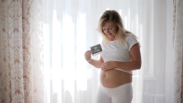 Ultraljud foto av spädbarn i handen på förväntad kvinna bredvid naken gravid mage — Stockvideo