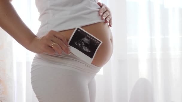 Vrouw massages haar grote buik in slow motion en houdt scan van toekomstige baby in de buurt van buik — Stockvideo