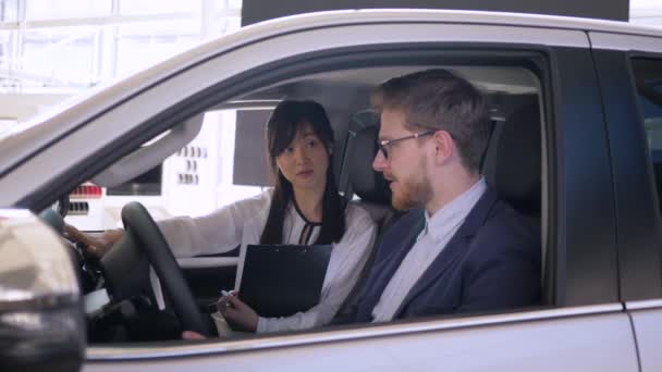 Auto-Geschäft, erfolgreiche asiatische Autoverkäuferin berät Kerl Käufer sitzt im Auto gibt Schlüssel und schüttelt Hände im Autohaus Nahaufnahme — Stockvideo