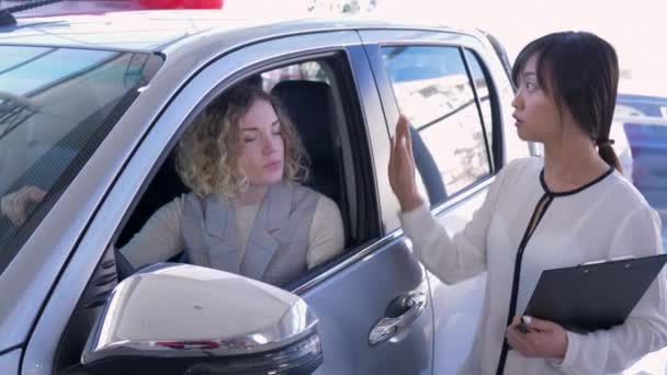 自動車ビジネス、アジアの女性の車の売り手は、ショールームで成功した販売後、車の中でクライアントの女の子とキーの上に手を相談 — ストック動画