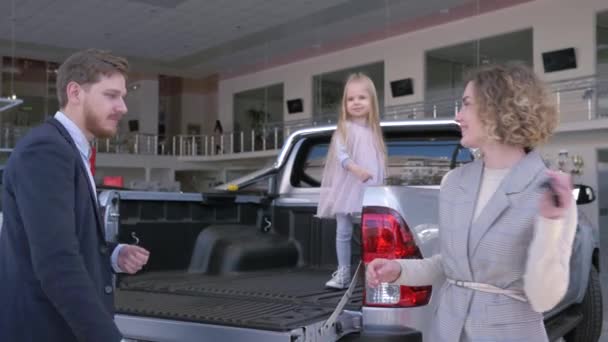 Счастливая покупка автомобиля, веселая молодая семья с ребенком девушка смешные танцы с ключами при покупке автомобиля в автосалоне — стоковое видео