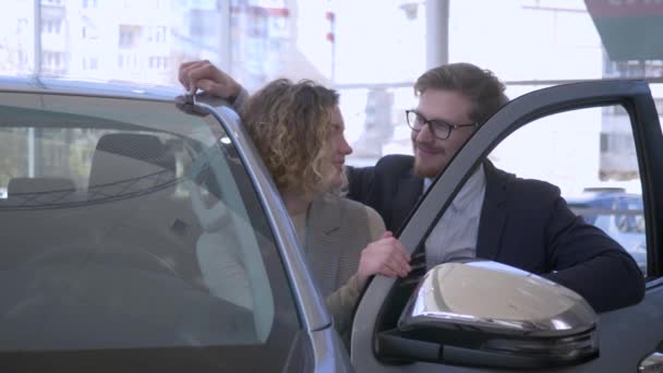 車の購入、笑顔のカップルの愛の新しい車の所有者は、自動車店でキーを購入し、ショーを楽しむ — ストック動画