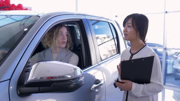 Portrait of professional car seller hands over keys woman client inside vehicle while buying automobile at dealership — Stock Video