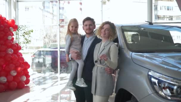 Heureux client de la famille dans le concessionnaire automobile, portrait de parents souriants avec petite fille enfant sur les mains montre les clés de l'automobile achetée au magasin d'automobiles — Video