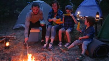 Amerikan ailesi tuzla mısır yer, kamp yapar, ormanda piknik yapar, anne, baba ve oğullar taze sarı mısır yer.