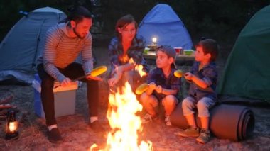 Ormanda piknik, ateşin etrafında Amerikan ailesi akşam sarı mısır hazırlayın, anne, çocuk ve baba yaz tatilinde.