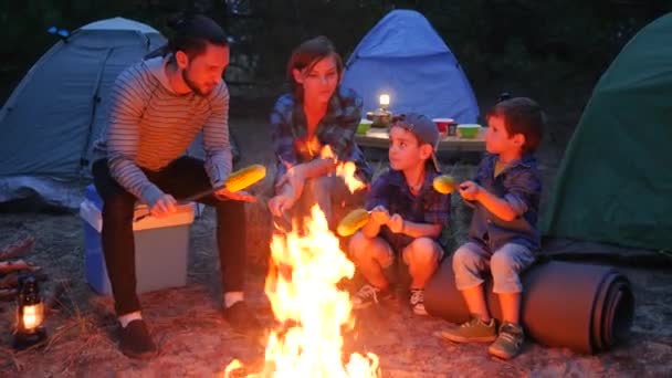 森林でのピクニック、火の周りのアメリカの家族は、夏休みの間、夕方、母、子供、父に黄色のトウモロコシを準備します。 — ストック動画