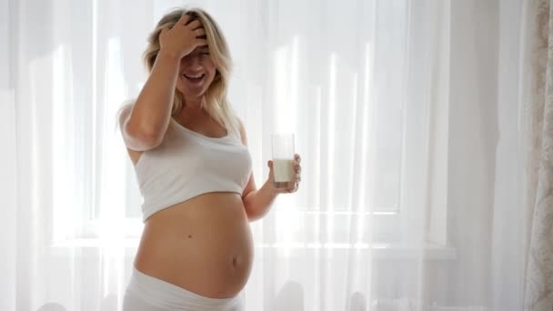 Future mommy keeps glass milk and rubbing tummy, pregnant woman looks in camera — Stock Video