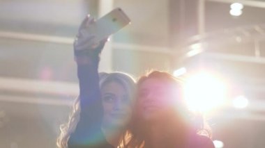 Çekici lüks kız arkadaşlar pahalı bir etkinliğin arka planında cep telefonuyla selfie çekiyorlar.