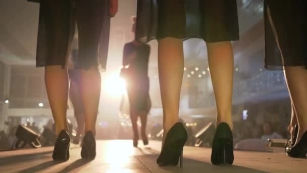 Вечер моды, тонкие ноги моделей в черных туфлях на высоких каблуках прогуливаются по подиуму ярким светом крупным планом на несфокусированном фоне во время презентации новой коллекции — стоковое видео