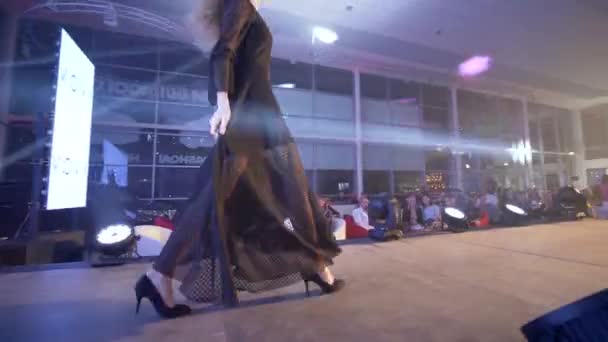 Laufsteg-Modelmädchen in schwarzem Abendkleid in Stöckelschuhen entweicht auf Podium bei Modeevent ins Scheinwerferlicht — Stockvideo