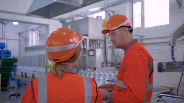Ingénieurs femelle avec l'homme dans des casques avec tablette numérique vérifient l'usine de production tout en discutant de la qualité du travail — Video
