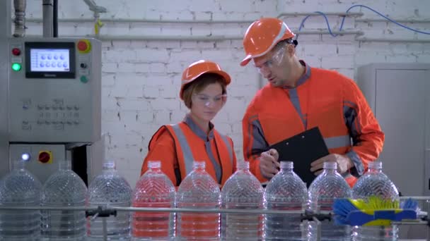 Ingenieure in Helm und Arbeitskleidung in der Nähe von Förderbändern zur Abfüllung von Mineralwasser in Plastikflaschen während der Inspektion und Qualitätskontrolle der Produktion — Stockvideo