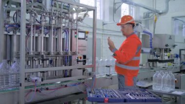 Profesyonel teknisyen erkek miğfer ve iş kıyafetleri. Fabrikada plastik şişelerde maden suyu şişelemek için kemer hattının yanında özel aletlerle yenileme tesisi ekipmanı kullanıyor.