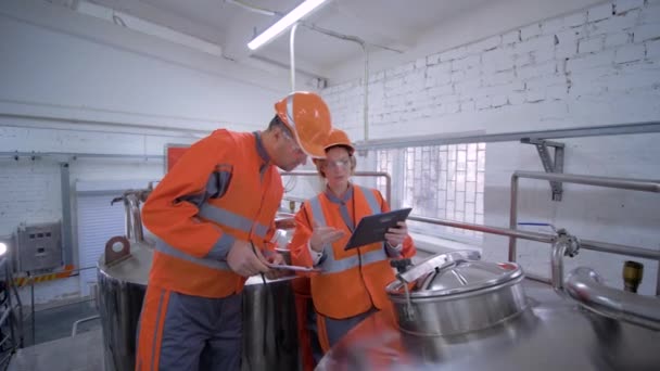 Factory Engineers woman with male in helmets with tablet laptop are checking production plant while discussing quality — Stock Video