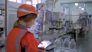 Ağır kadın işi, sert şapkalı fabrika uzmanı kız bilgisayar tabletini revizyon için kullanıyor ve donanım işlemini kontrol ediyor.