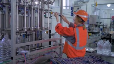 Ağır sanayide çalışan kadın, mutlu fabrika teknisyeni kadın, sert şapka takıyor, ekipmanları tamir ediyor ve bitkilere gülümsüyor.