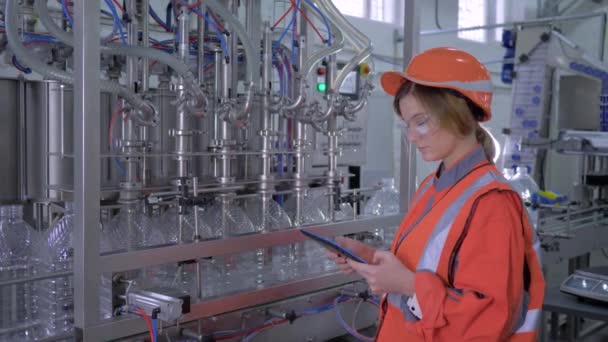 Modern technology at factory, Industry worker female into helmet uses digital tablet to control operation of conveyor line for bottling mineral water in bottles — Stock Video