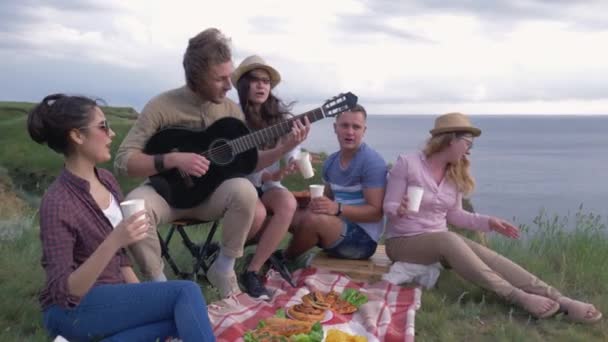 Joyfull weekend, vrolijke vrienden vrouw en man plezier hebben en gitaar spelen terwijl ontspannen op picknick partij in de natuur in de buurt van rivier — Stockvideo