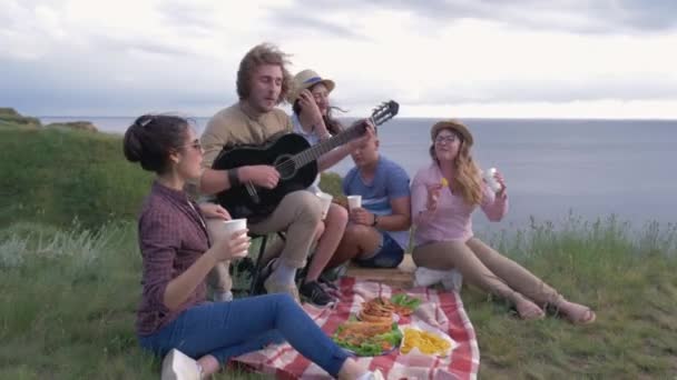 Freizeit im Freien, fröhliche Freunde Männer und Frauen spielen Musikinstrumente und singen Lieder beim Picknick im Freien in der Nähe des Flusses — Stockvideo