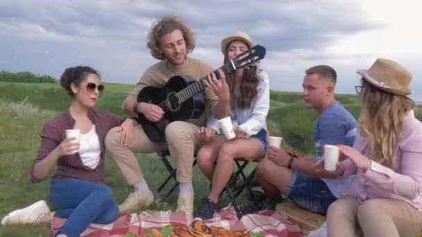 Picknick party, grappige vrienden en vriendinnen die plezier hebben en gitaar spelen terwijl ze buiten rusten in de buurt van zee — Stockvideo