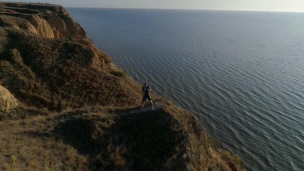 Fuerte boxeador macho realiza golpes puños ejercicio en la hermosa naturaleza cerca de agua brillante contra el cielo en la luz soleada brillante — Vídeo de stock