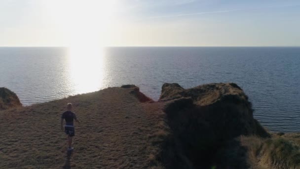 Entrenamiento deportivo al aire libre, el hombre en ropa deportiva camina sobre la pendiente al agua en la naturaleza contra el cielo a la luz del sol brillante — Vídeo de stock