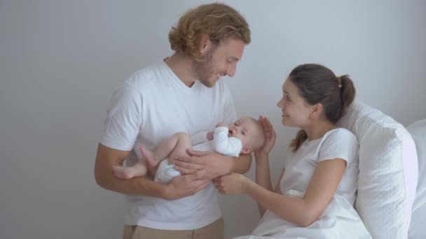 Щаслива молода мати з батьком тримає маленьку дитину в руках і посміхається в світлій камерній клініці — стокове відео