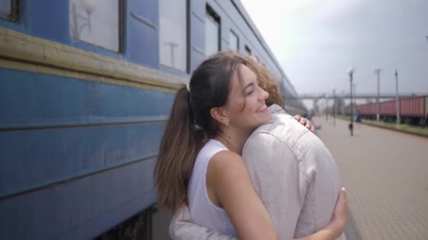 Радость счастливой молодой женщины обнимает мужчину и смеется возле железнодорожного вагона на вокзале после разлуки — стоковое видео