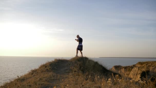 Sports training on open air, muscular pugilist male practicing boxer punches before sparring on workout on hill near sea — Stock Video