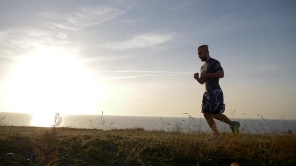Sports run, muscular guy moves on meadow of river against sky — Stock Video