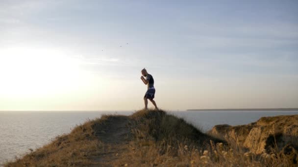 Entrenamiento deportivo al aire libre, joven luchador practicando golpes antes de la competencia en el entrenamiento en la colina cerca del río — Vídeo de stock