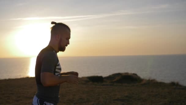 Sports guy runs in slow motion on seashore against of water and sky at sunset — Stock Video